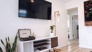 Una sala de estar moderna con un televisor de pantalla plana montado en la pared, un mueble blanco para entretenimiento con una planta y piso de madera.