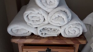 Une pile de serviettes blanches est posée sur une table de chevet en bois, qui est dotée d’un tiroir.