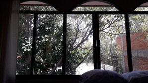 Une pièce dotée d’une grande fenêtre donnant sur un arbre et un mur de briques.