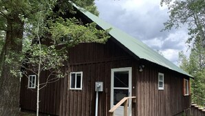 Eine rustikale Holzhütte mit einem grünen Dach, einer Haustür und einer Holztreppe, die zu ihr hinaufführt.