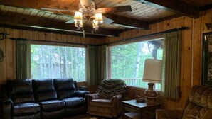 Ein gemütliches Blockhaushaus-Interieur mit einem Ledersofa, Sesseln, einem gemusterten Teppich und einem Deckenventilator.