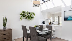 Een moderne eethoek met een glazen tafel, gestreepte stoelen, een potplant en uitzicht op de keuken.