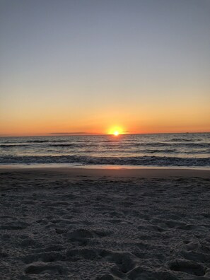 Ein Strand bei Sonnenuntergang mit Wellen und einem klaren Himmel.