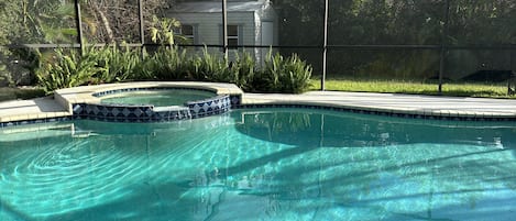 A clear swimming pool with a tiled edge, surrounded by a fence and lush greenery.