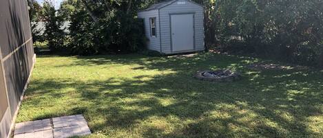 A backyard with a shed, a fire pit, and a lawn.