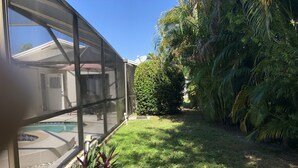 A modern house with a glass-enclosed patio, a swimming pool, and lush greenery. - Beach / Pool Oasis in Beautiful Naples, Fl. (Naples)