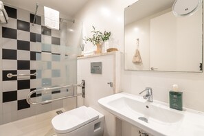 Un baño con pared de baldosas a cuadros, un lavabo blanco, un espejo y un inodoro.