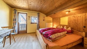 Une chambre dans une cabane en bois, avec un lit, un bureau en bois, une chaise et une fenêtre avec des rideaux.