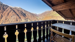 Un balcon en bois, agrémenté d’une table et de chaises, qui offre une vue sur un paysage montagneux aux sommets enneigés.