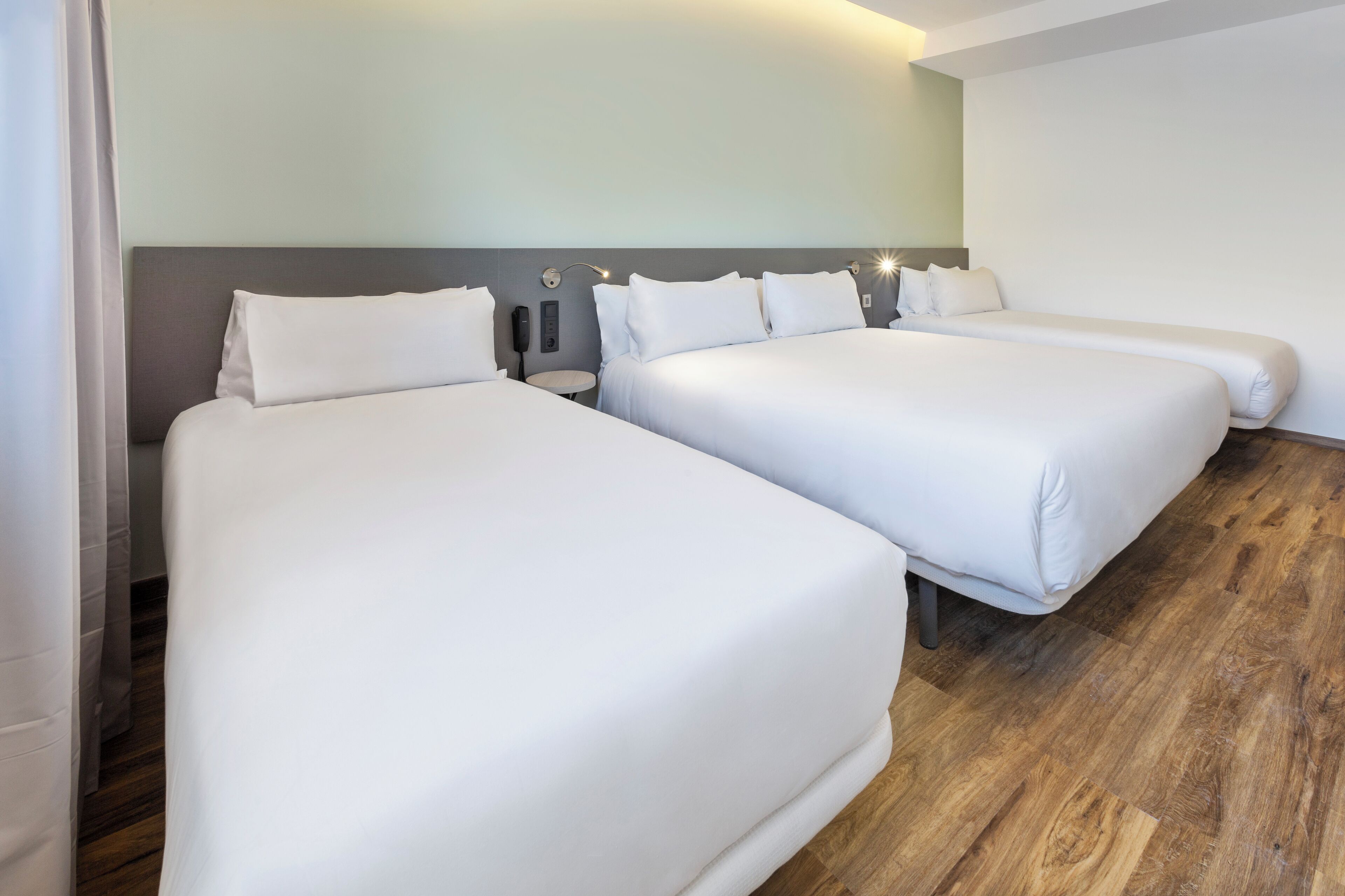 A hotel room with two single beds, a nightstand with a lamp, and a wooden floor.