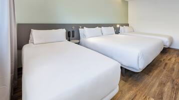 A hotel room with two single beds, a nightstand with a lamp, and a wooden floor.