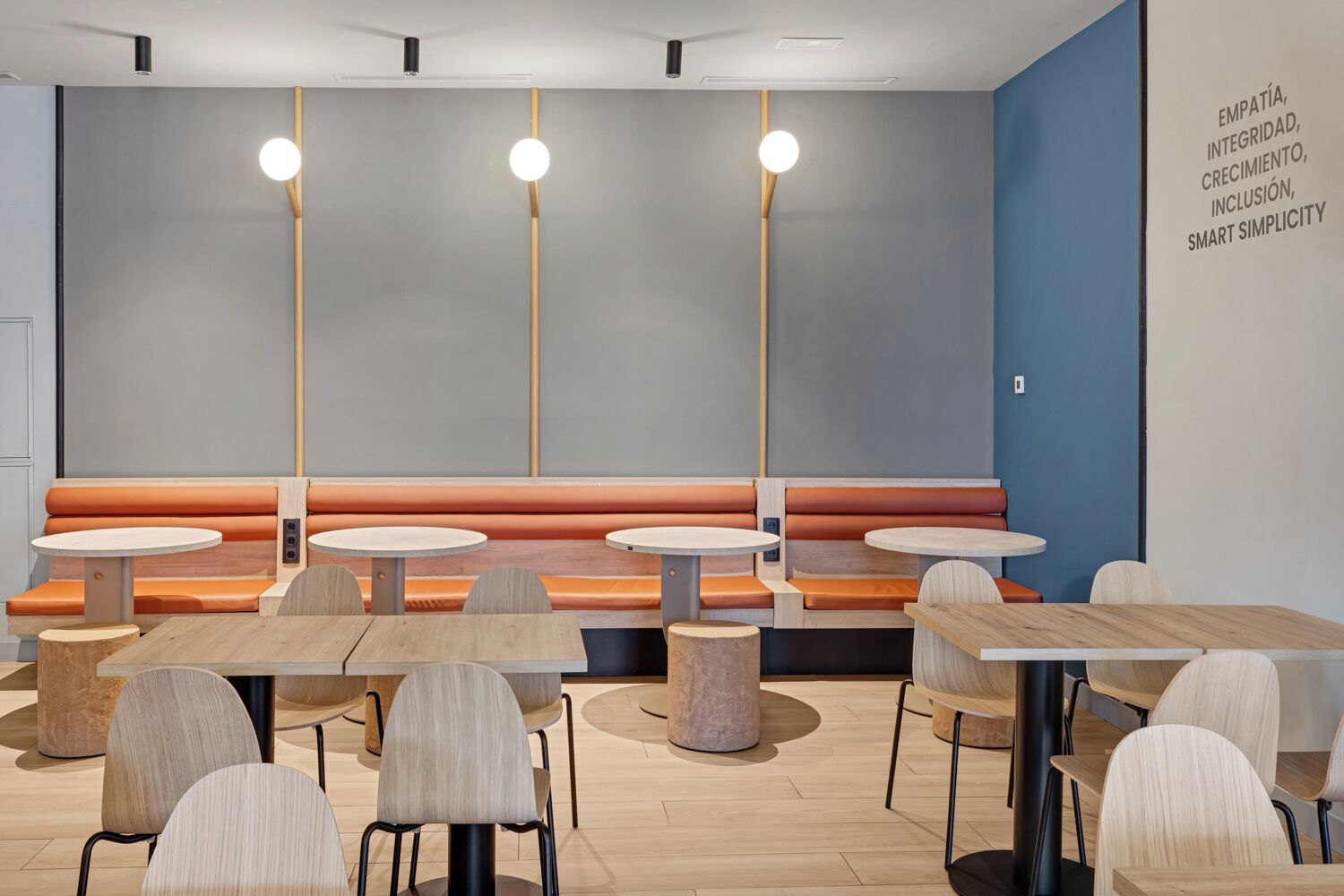 A modern restaurant with round tables and orange cushioned booths.