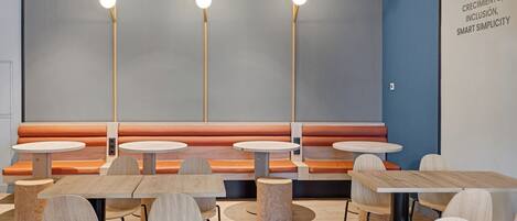 A modern restaurant with round tables and orange cushioned booths.