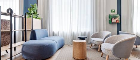 Una sala de estar moderna con un sofá azul, sillones grises, una mesa de centro redonda de madera y una mesita auxiliar.