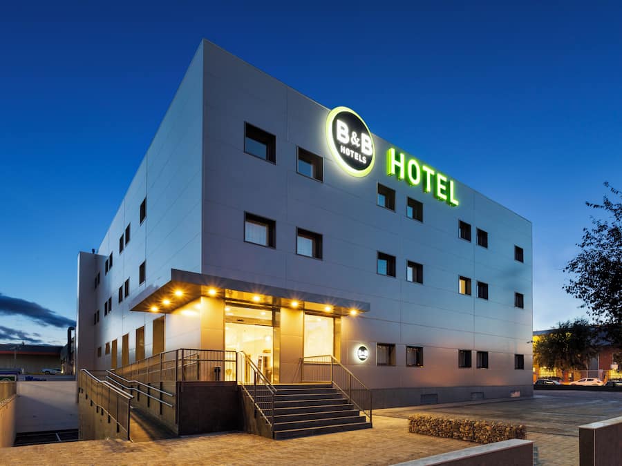 Un hôtel-chambre d’hôtes moderne, doté d’une enseigne lumineuse bien visible, d’un escalier menant à l’entrée et d’une façade bien éclairée.
