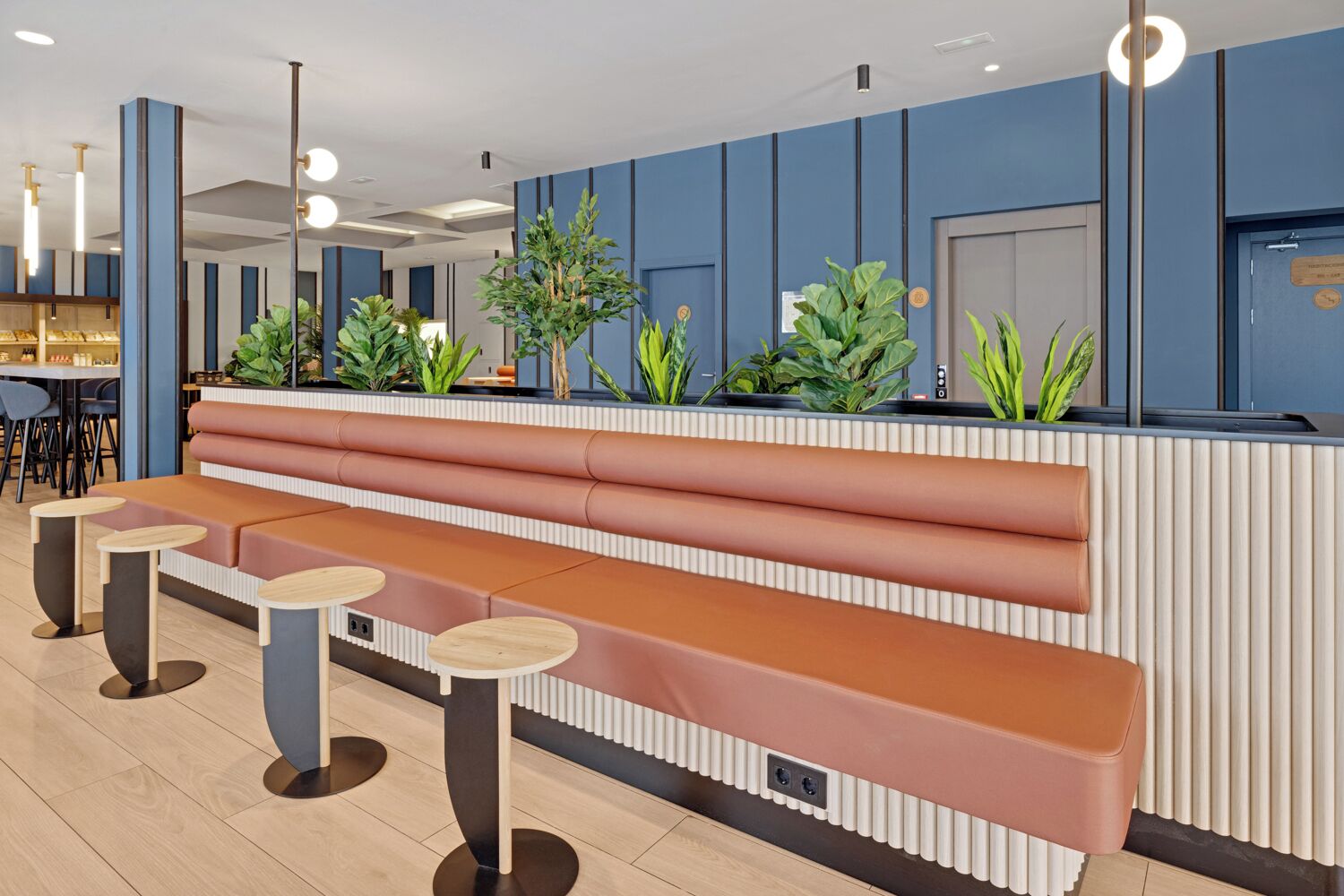 Un área de recepción moderna con un banco y mesas, paredes azules y plantas en macetas.