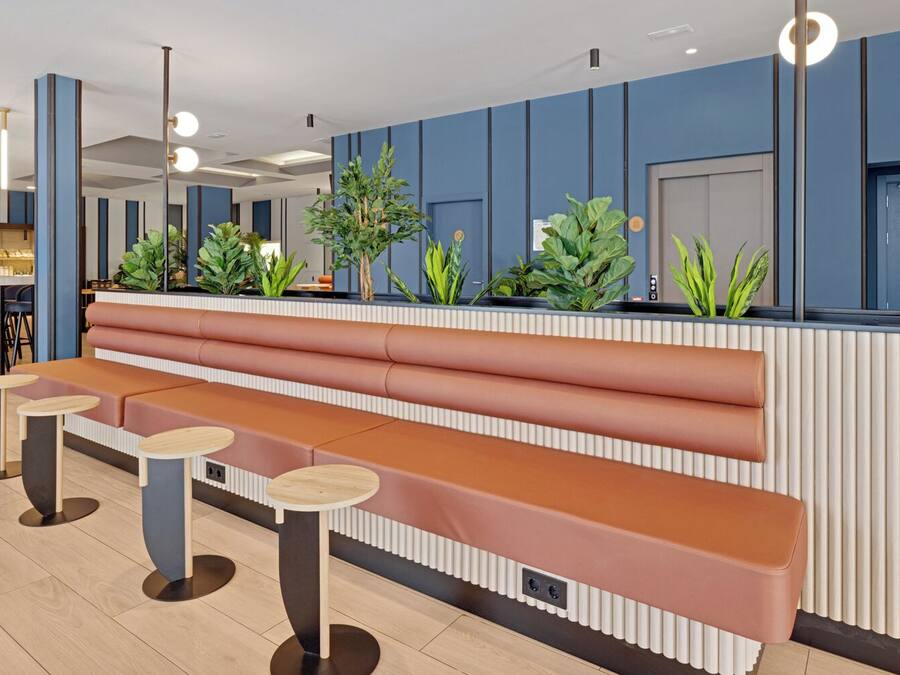 Un área de recepción moderna con un banco y mesas, paredes azules y plantas en macetas.