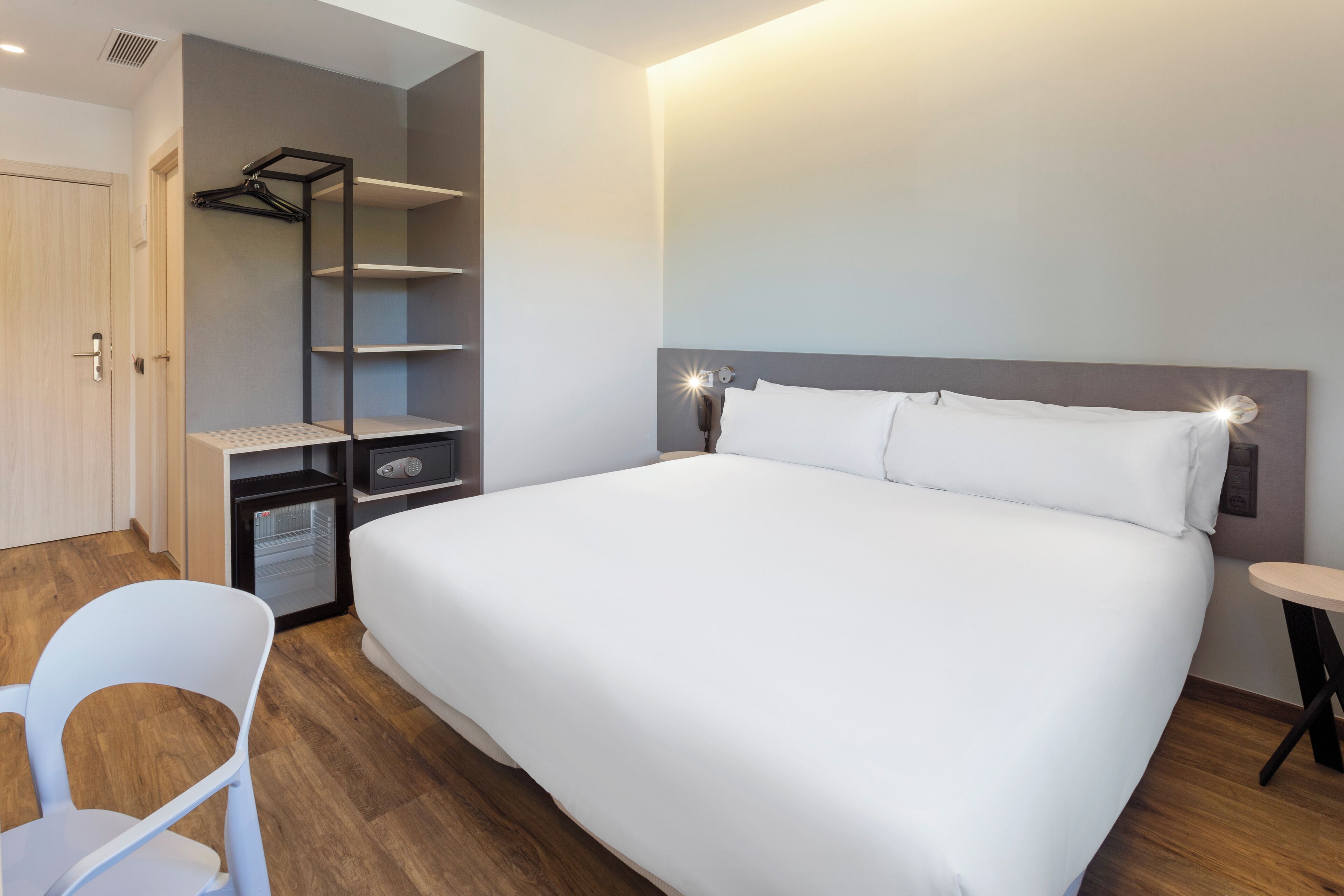 Ein Hotelzimmer mit einem großen Bett, einem Schreibtisch mit Stuhl, einem Kleiderschrank und einem kleinen Kühlschrank.