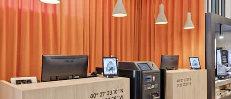 A reception desk with two monitors, a self-service kiosk, and a digital display.