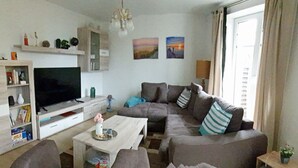 Ein Wohnzimmer mit Fernseher, Sofa, Couchtisch und Regalen mit diversen Gegenständen.
