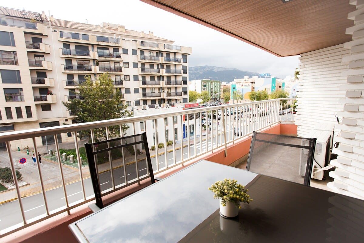 Varanda com mesa e cadeiras, um vaso de planta e vista para o horizonte urbano, com edifícios e uma montanha ao longe.