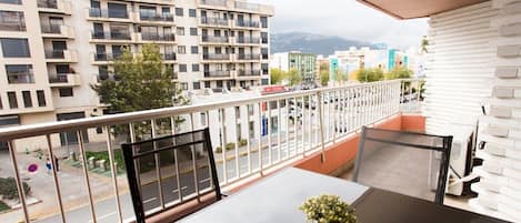 Varanda com mesa e cadeiras, um vaso de planta e vista para o horizonte urbano, com edifícios e uma montanha ao longe.