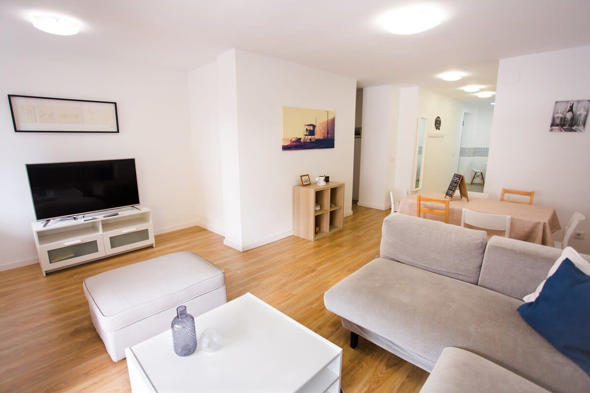 A modern living room with a flat-screen TV, a sofa, a coffee table, and a dining area with a table and chairs.