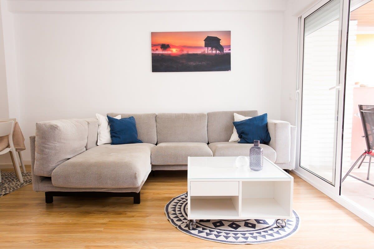 A living room with a beige sofa, a glass coffee table, and a painting on the wall.