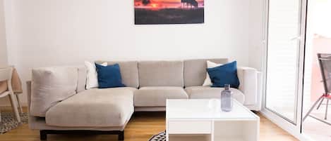 A living room with a beige sofa, a glass coffee table, and a painting on the wall.