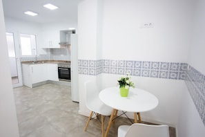 A modern kitchen with white cabinets, a built-in oven, and a dining area with a round table and two chairs. - Port-Front Balcony | Sea & Mountain Views (Dénia)
