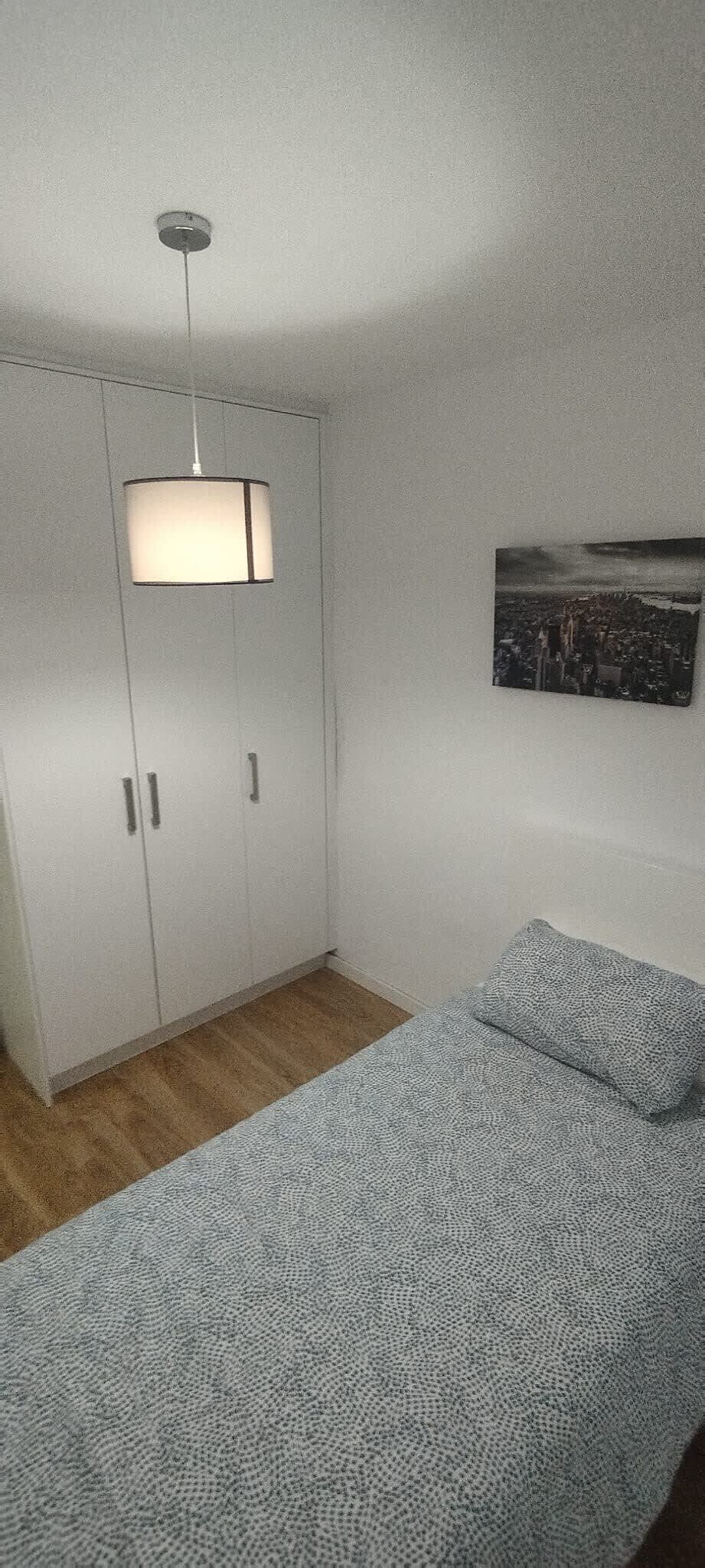 Una stanza con un letto, un armadio, una lampada a sospensione e un quadro appeso al muro.