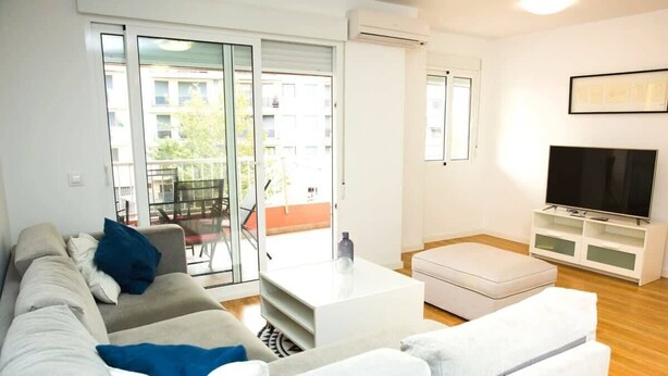 Una sala de estar moderna con un sofá, una mesa de centro, un televisor y un ventanal corredero que da a un balcón exterior.