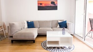 Una sala de estar con un sofá seccional color beige, una mesa de centro blanca y un cuadro de un atardecer en la pared.