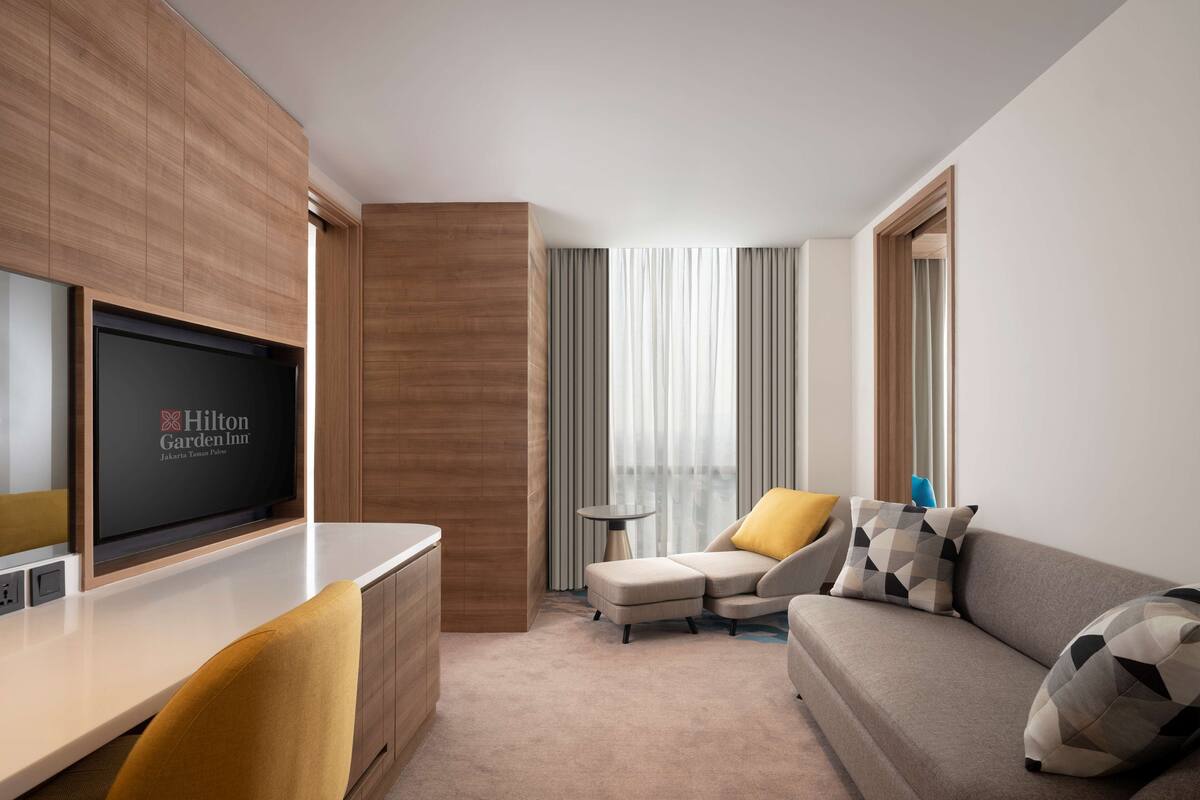 Una habitación de hotel moderna con una televisión de pantalla plana, un sofá, una silla y una mesita auxiliar.