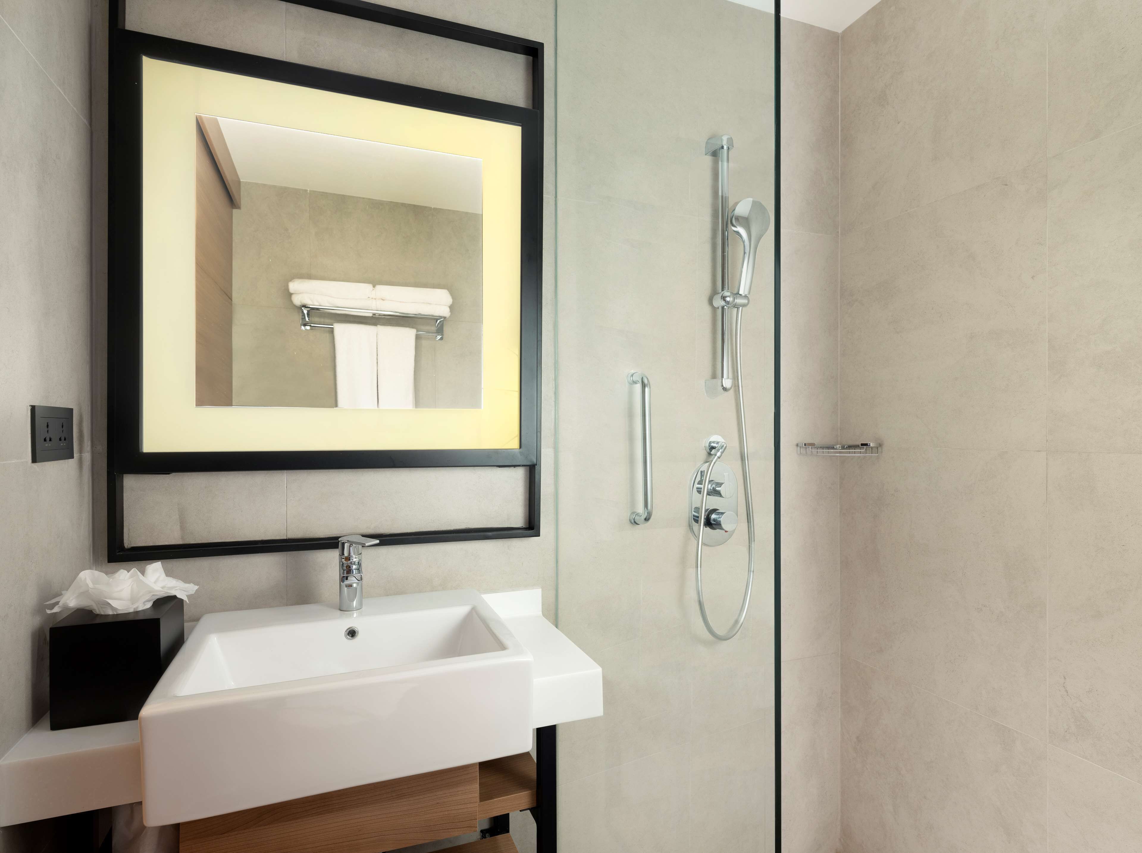 Un baño moderno con un lavabo blanco, un espejo enmarcado y una zona de ducha con mampara de cristal.
