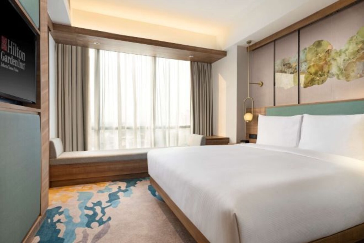 Une chambre d’hôtel avec un grand lit, une fenêtre avec des rideaux, un téléviseur fixé au mur et un tapis à motifs.