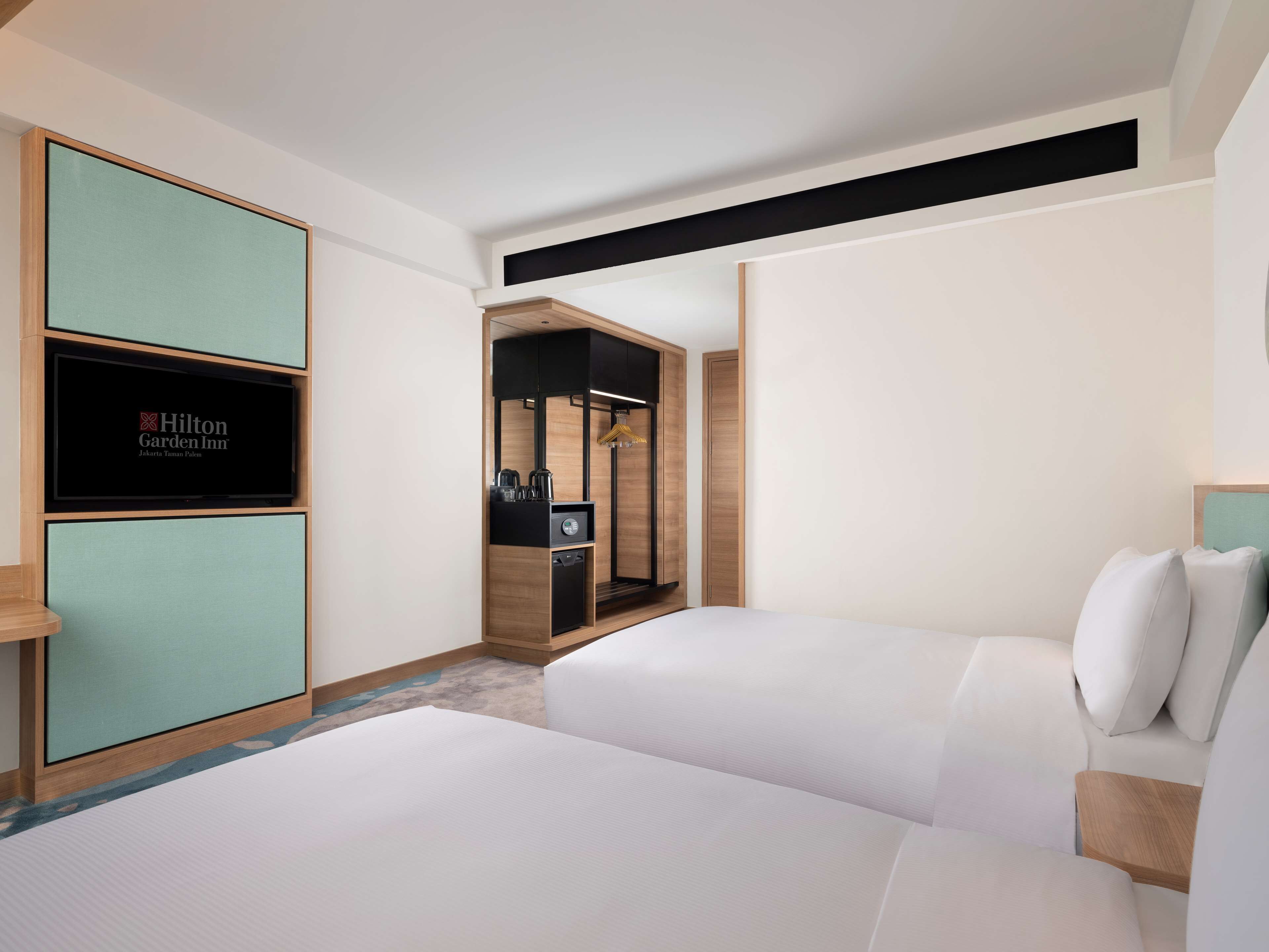 Une chambre d’hôtel avec deux lits, un minibar, un téléviseur affichant le logo de l’hôtel Hilton Garden Inn et un dressing.