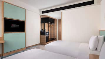 A hotel room with two beds, a minibar, a television displaying the Hilton Garden Inn logo, and a walk-in closet.
