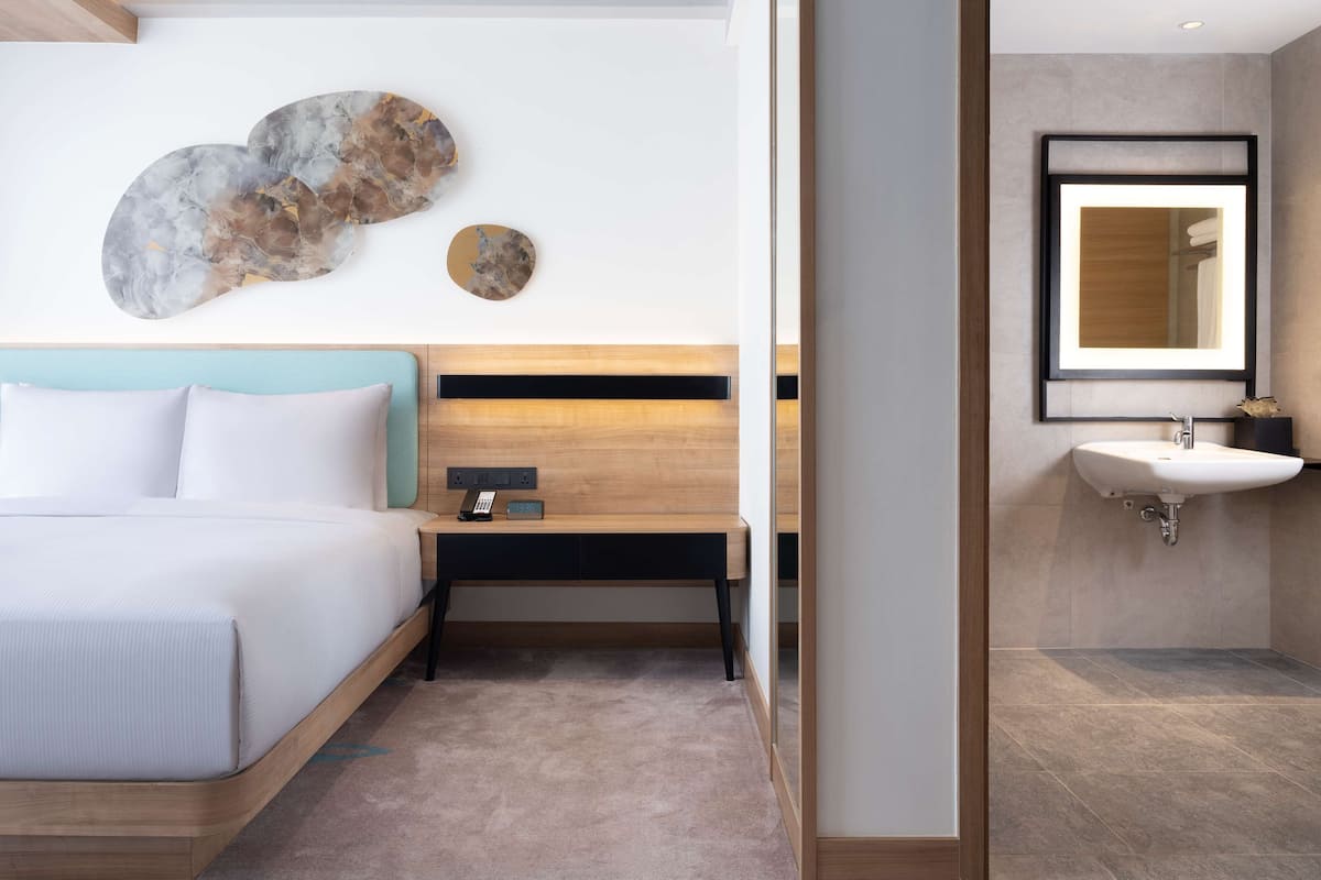 Una habitación de hotel moderna con cama, mesita de noche y un espejo grande.