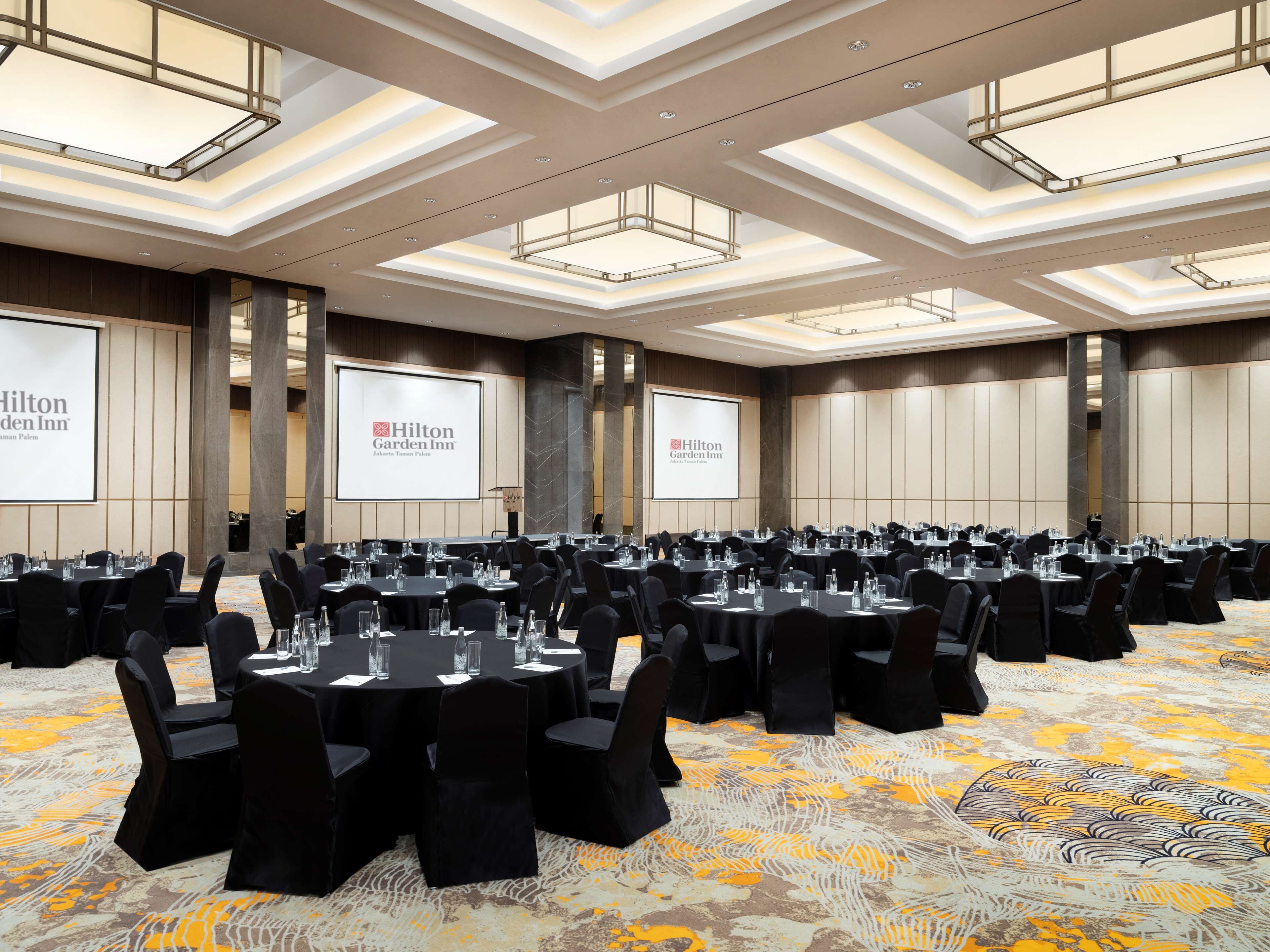 A conference room with multiple tables, black chairs, and a carpeted floor.