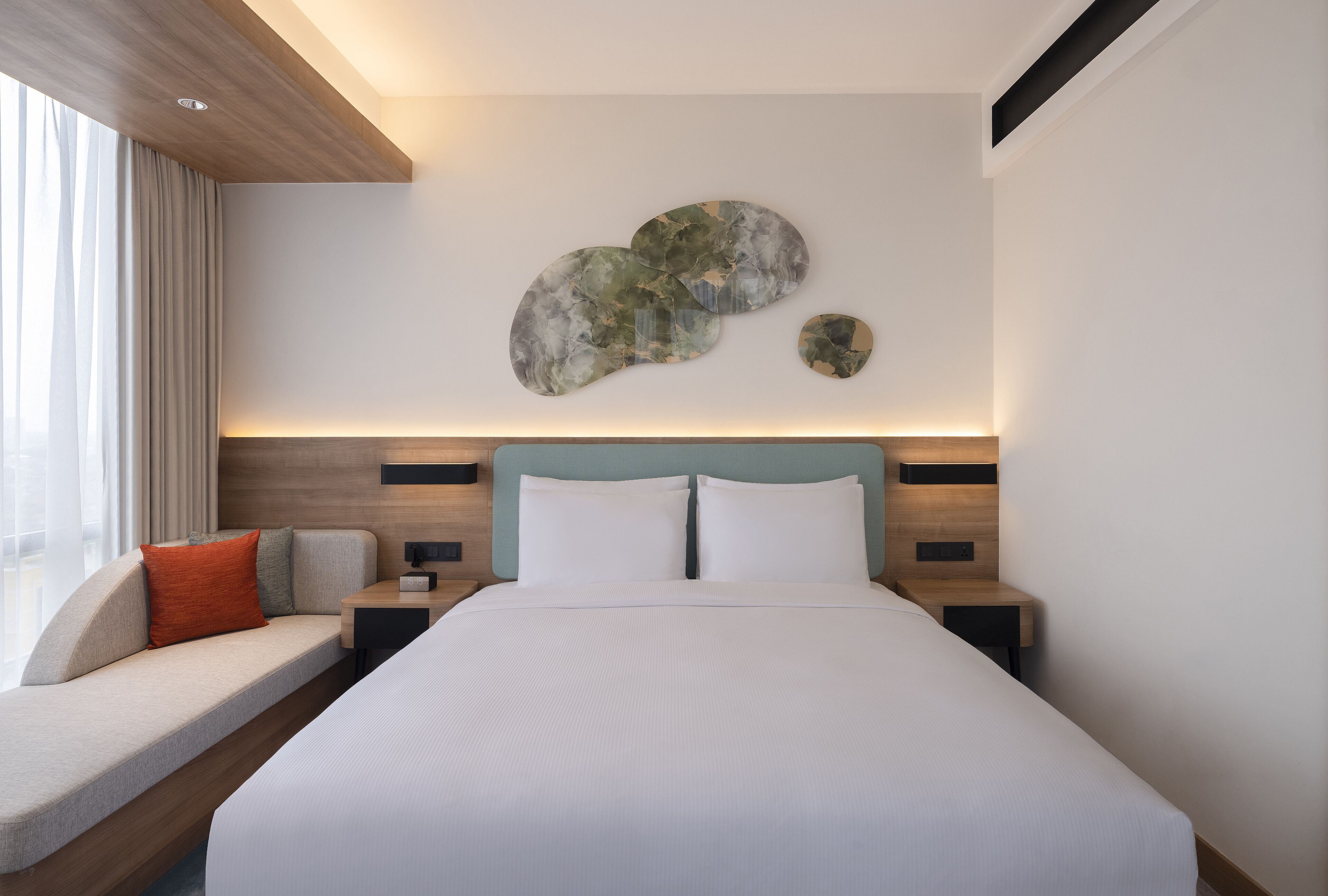 A modern hotel room with a large bed, a seating area with a view, and a unique wall art piece.