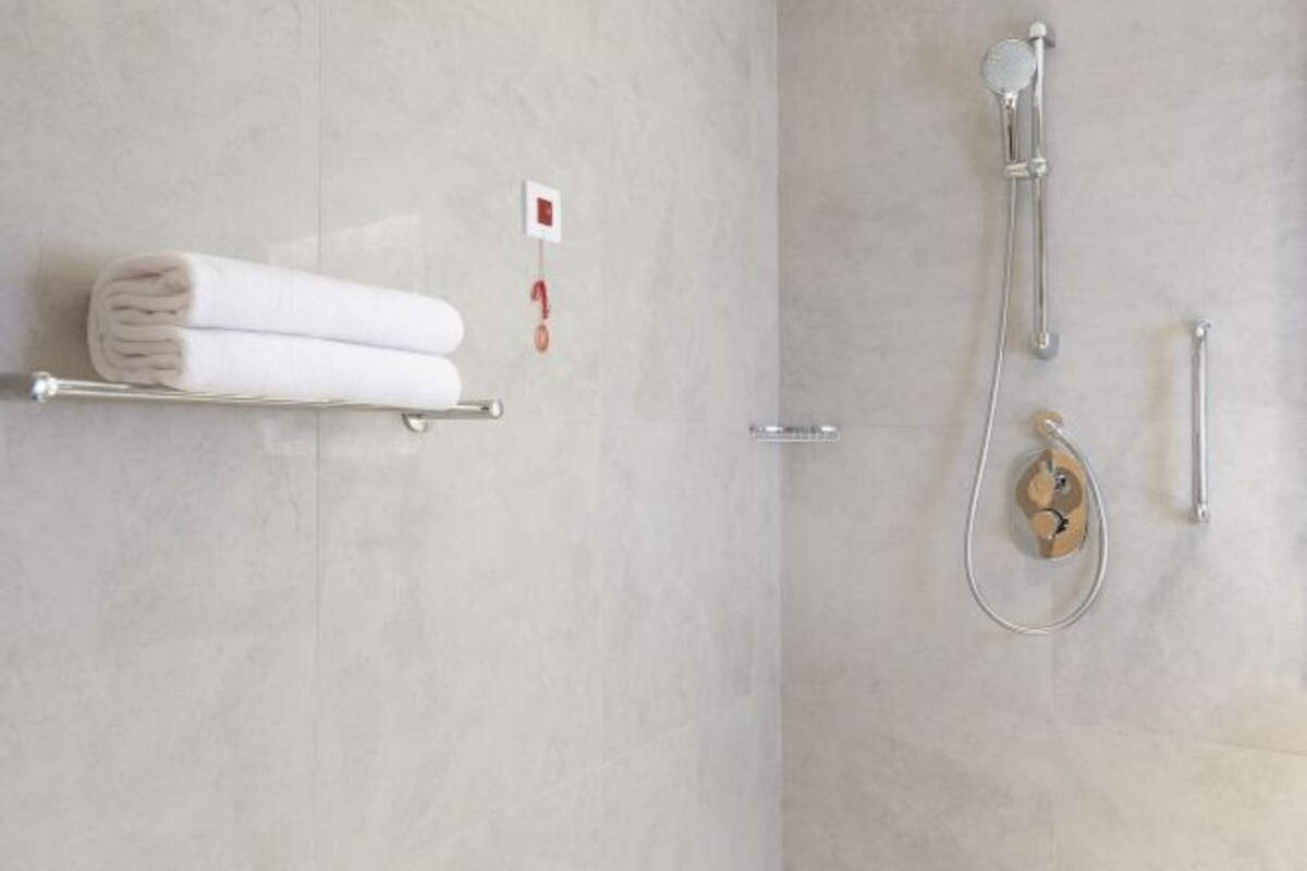 Une salle de bain équipée d’un porte-serviettes sur lequel sont pliés deux serviettes, d’une douche avec un pommeau de douche amovible et d’un panneau de commande fixé au mur.