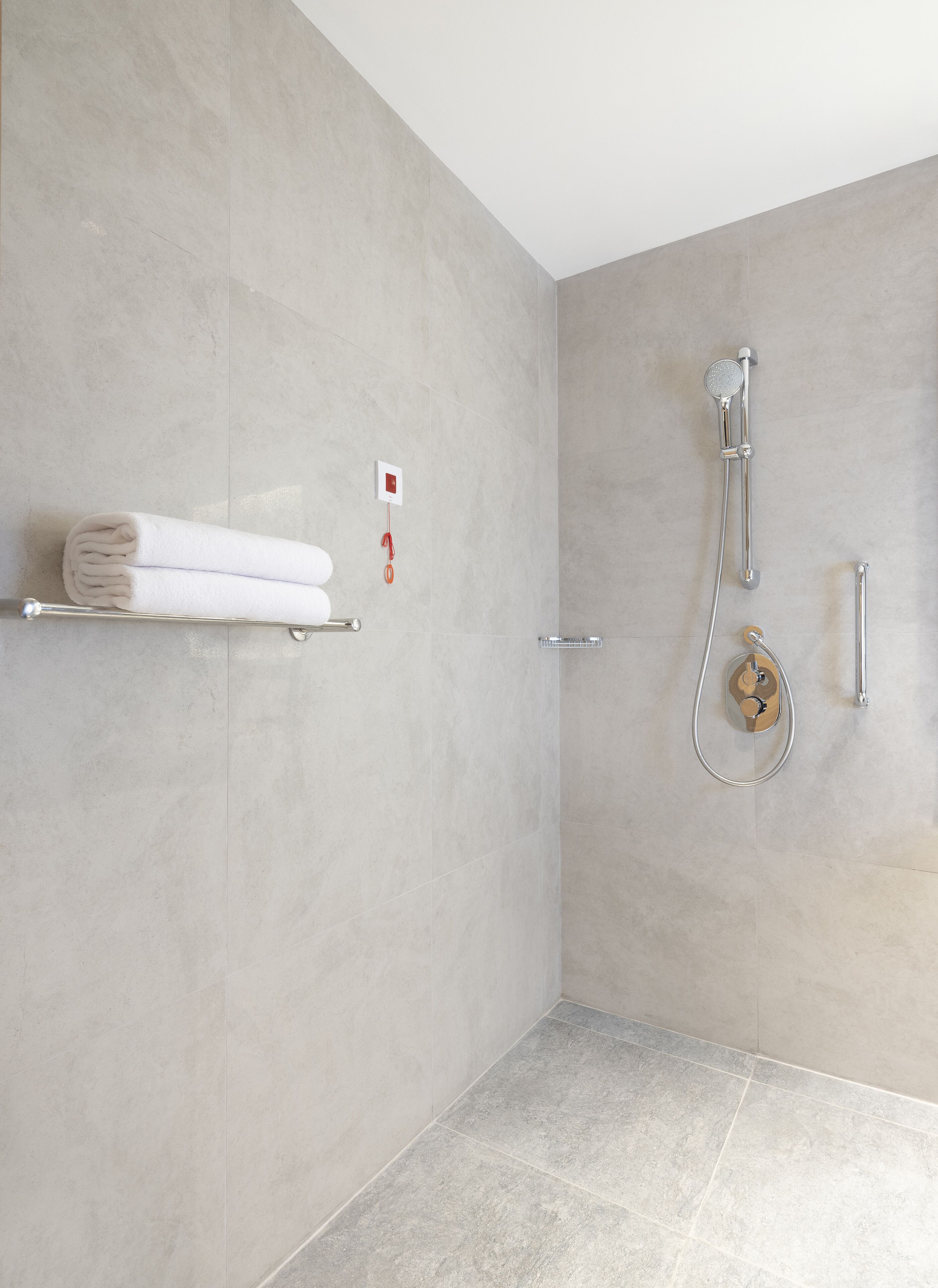 A modern bathroom with a walk-in shower, a towel rack with folded towels, and a control panel on the wall.