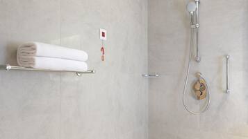 A modern bathroom with a walk-in shower, a towel rack with folded towels, and a control panel on the wall.