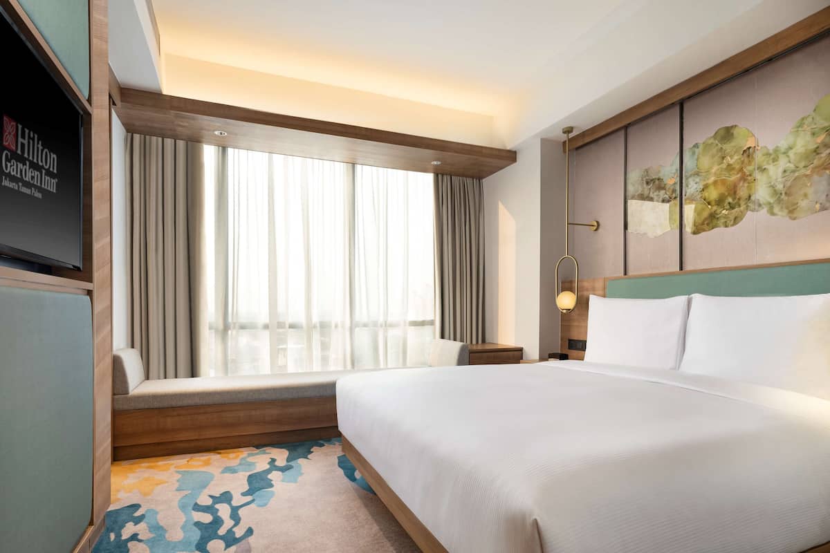Habitación de hotel con una cama grande, zona de estar con vistas a la ciudad, televisión de pantalla plana y una obra de arte moderno en la pared.