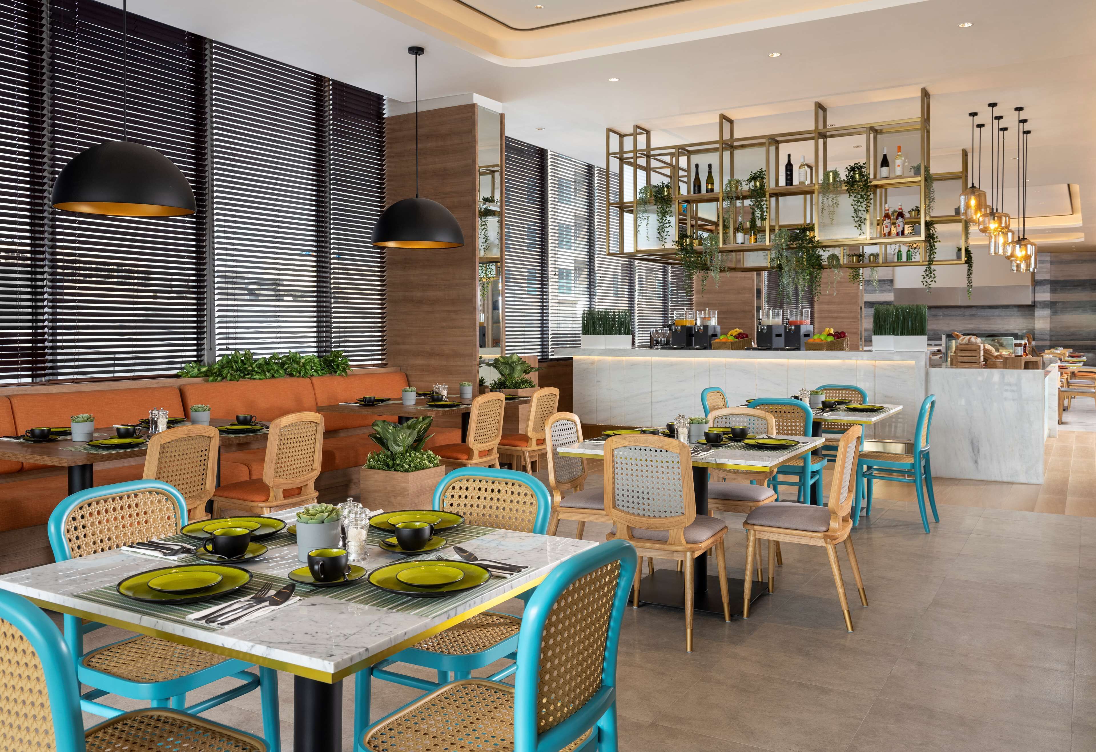 Un restaurante moderno con una zona de bar, muebles de madera y una variedad de plantas.