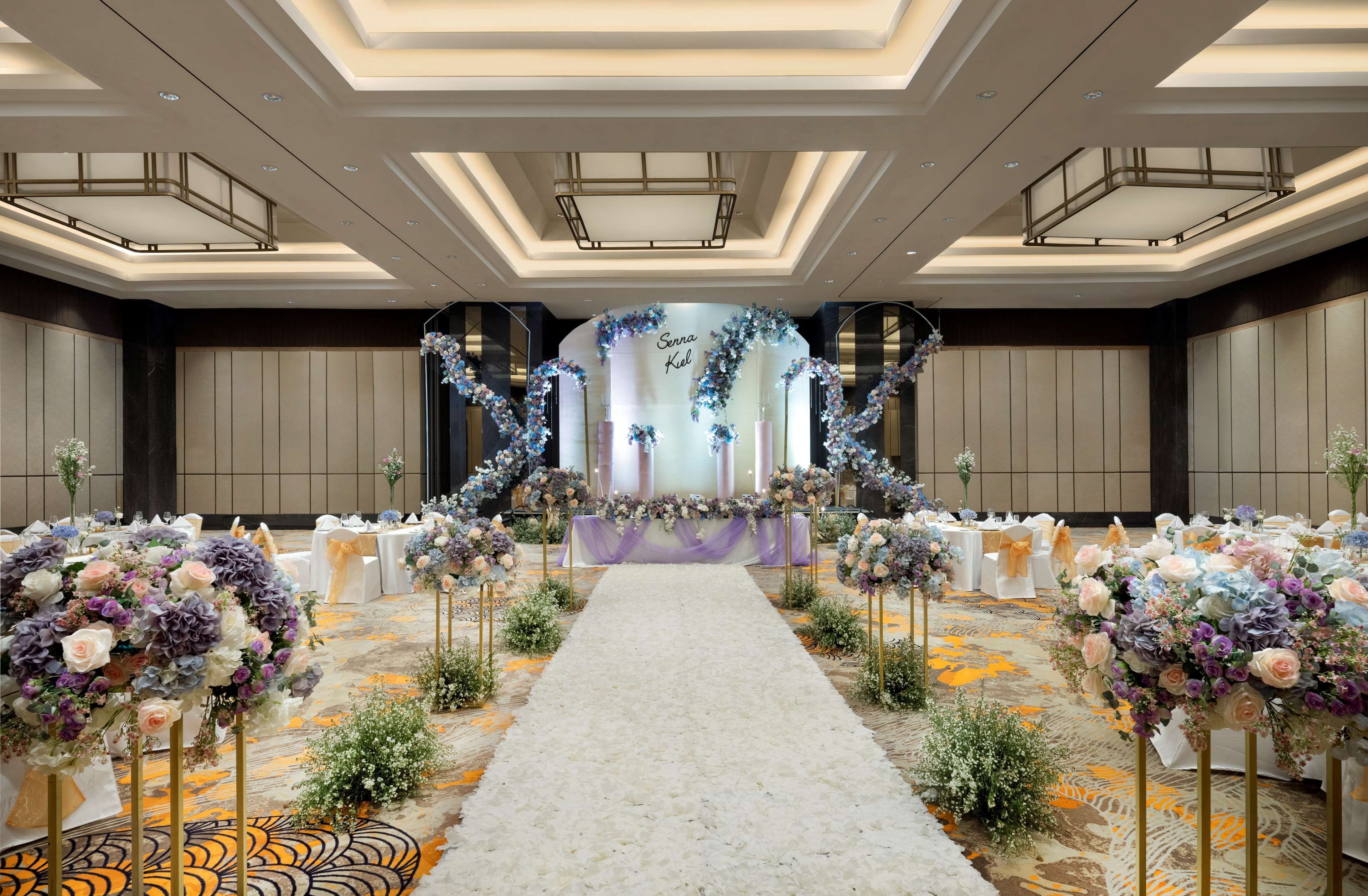 Un vaste hall doté d’une scène centrale, d’un tapis blanc et de compositions florales.