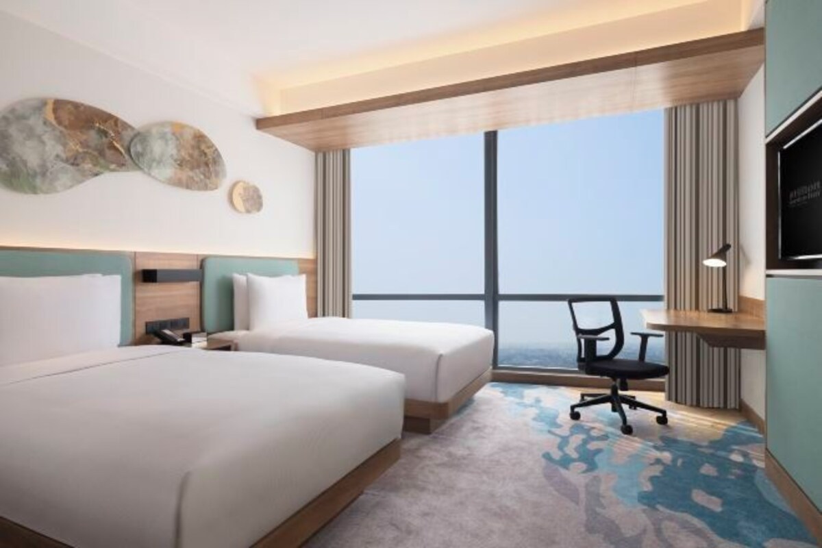 Une chambre d’hôtel avec deux lits, un bureau, une chaise et une grande fenêtre donnant sur un paysage agréable.