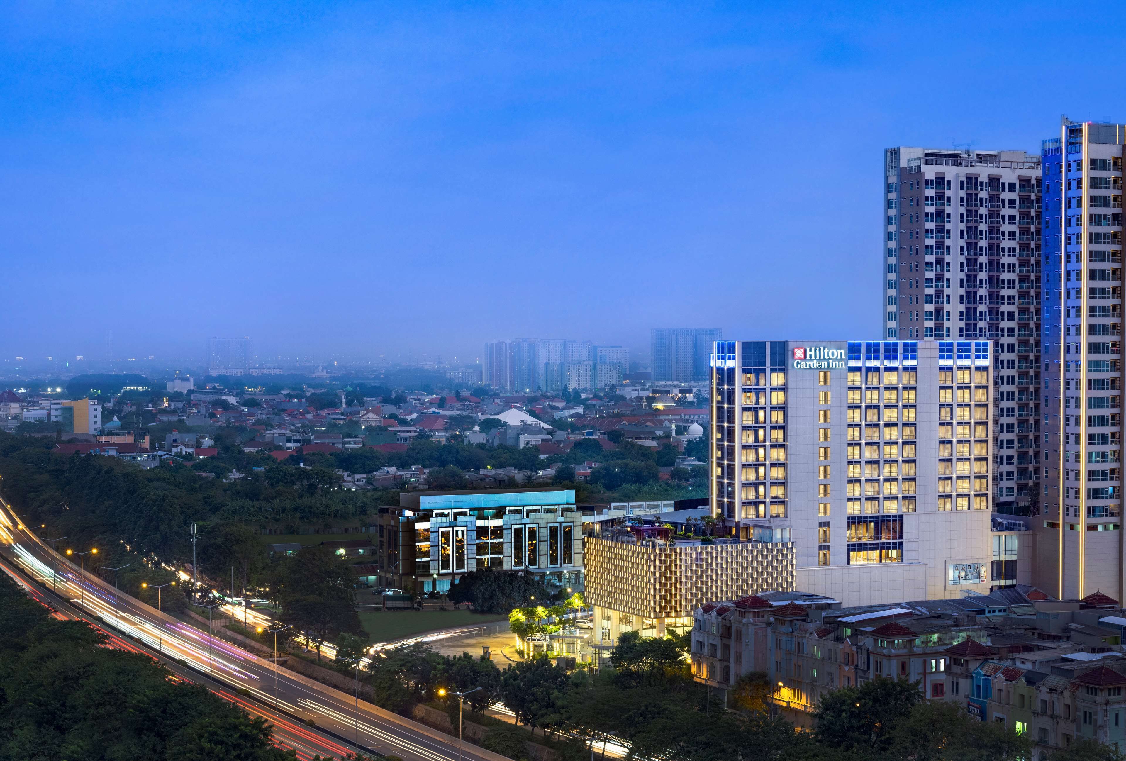 Un hotel de gran altura con diseño moderno, varios pisos y un llamativo letrero de Hilton Garden Inn.