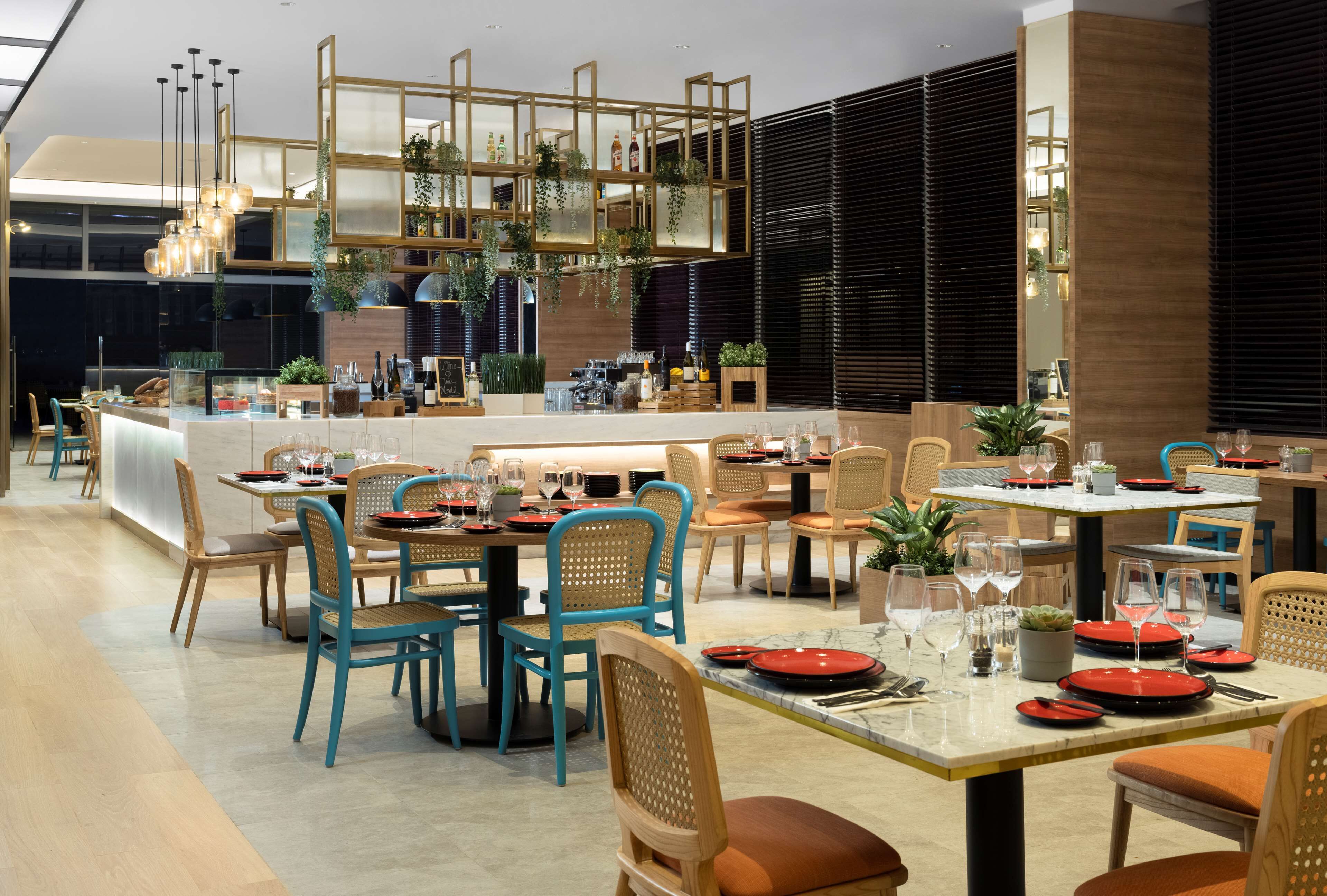 Um restaurante moderno com várias áreas de refeição, mobiliário de madeira e diversas plantas.